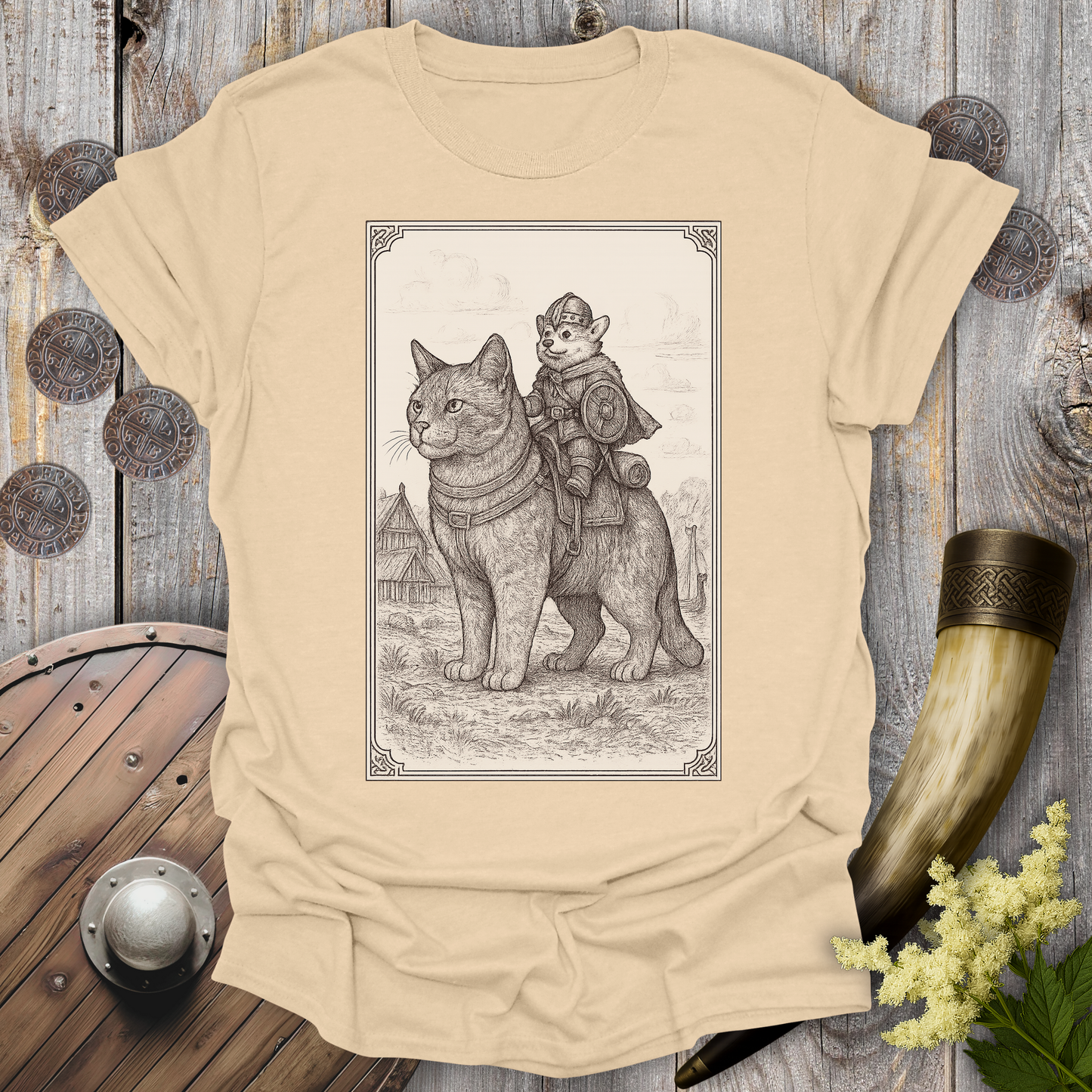 Beige Sand colored t-shirt with a beige and black graphic of a large cat and a Corgi Viking Dog riding it, in a Medieval Viking Age setting.