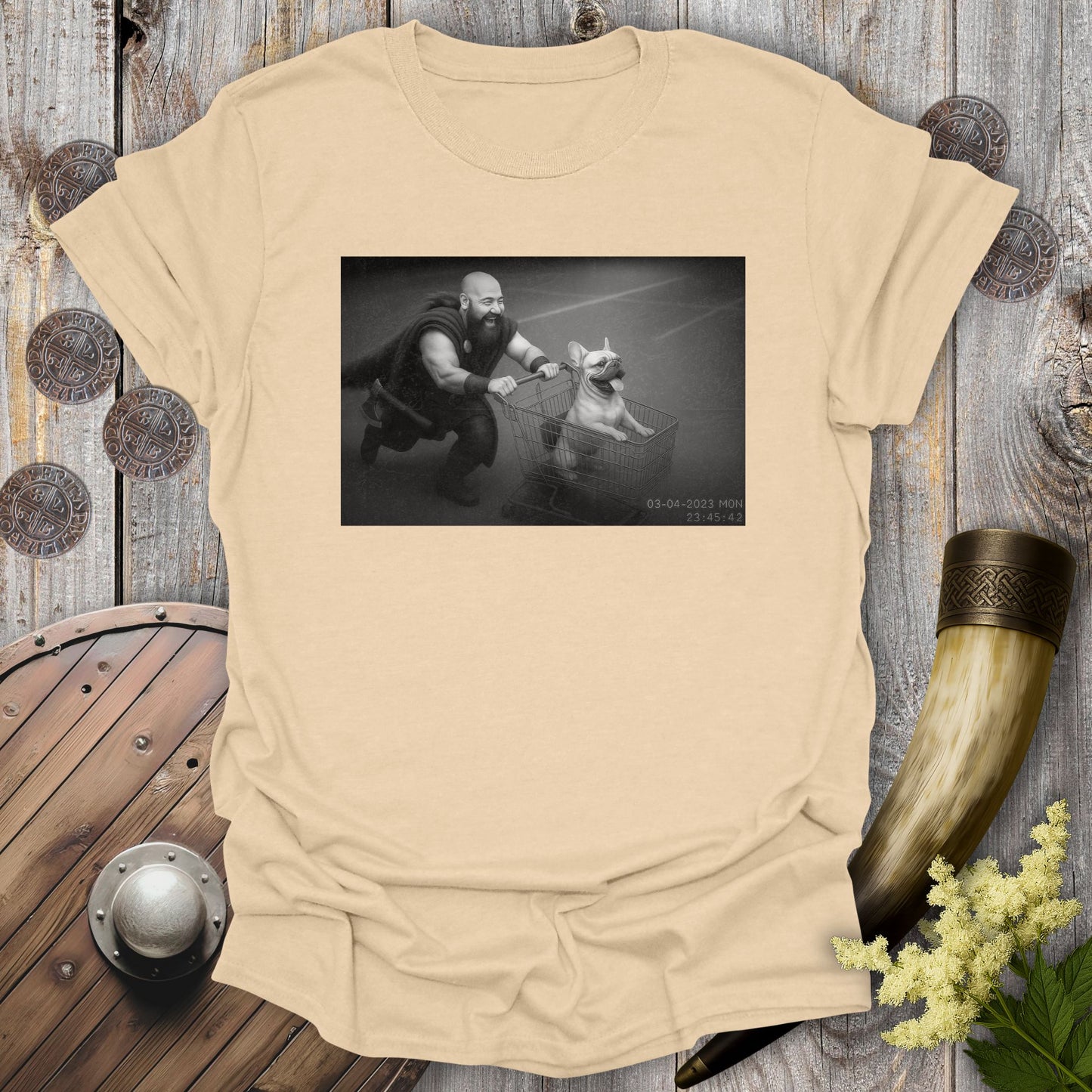 Beige Sand colored t-shirt with a graphic of a Viking and a Bulldog in a shopping cart, sprinting on a parking Lot.