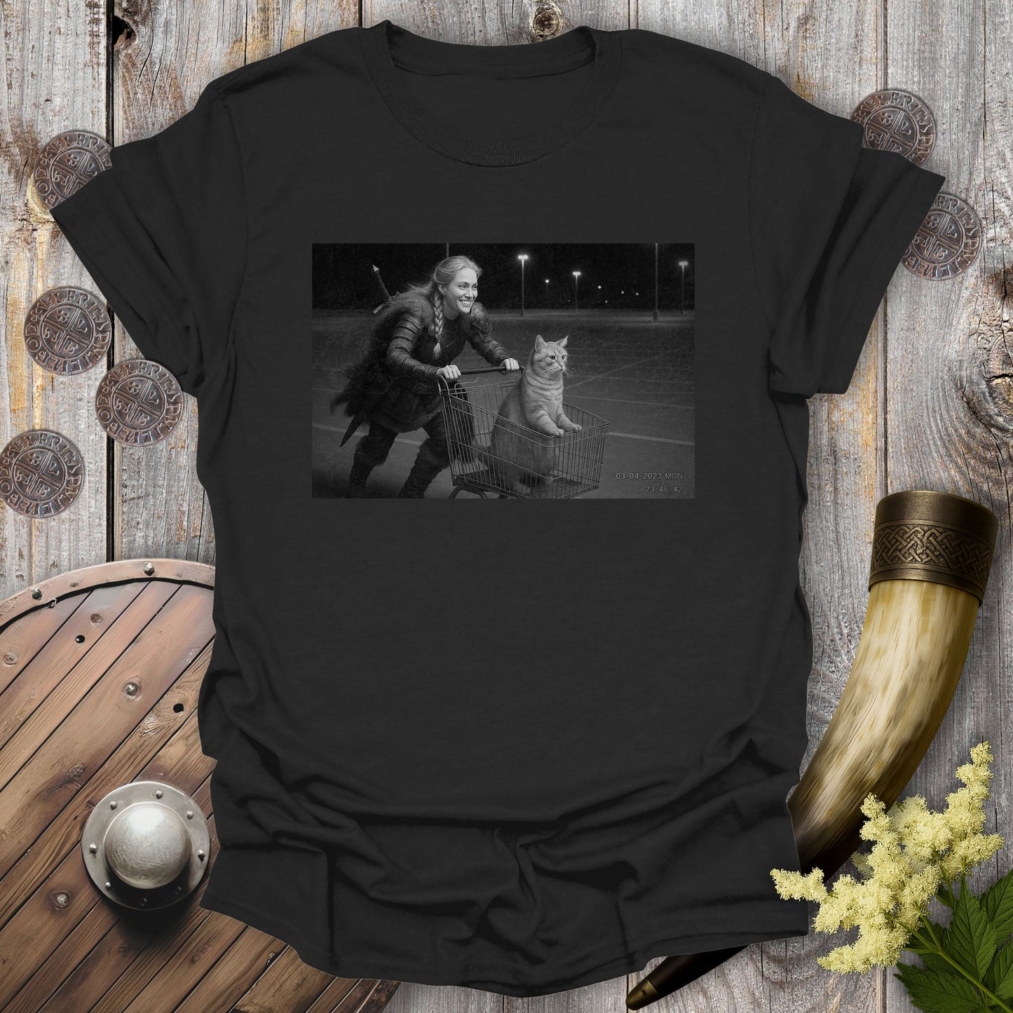 Black t-shirt with a graphic of a Viking Shieldmaiden and a tabby cat in a shopping cart, sprinting on a parking Lot.
