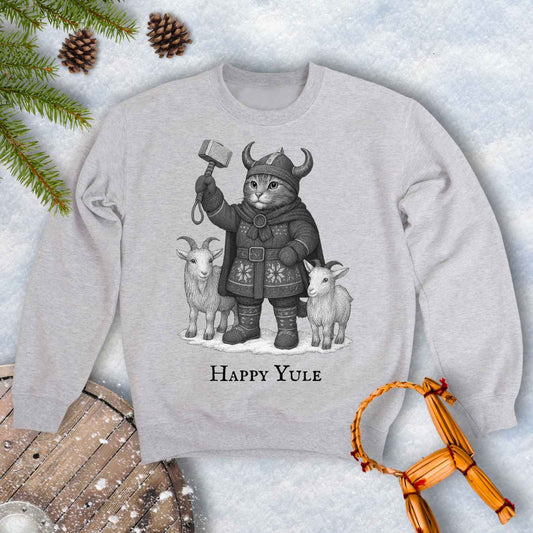 Gray ash colored sweatshirt with a black and white graphic of a Viking cat in winter gear, holding hammer Mjölnir, surrounded by two goats. 'Happy Yule' text under the image.