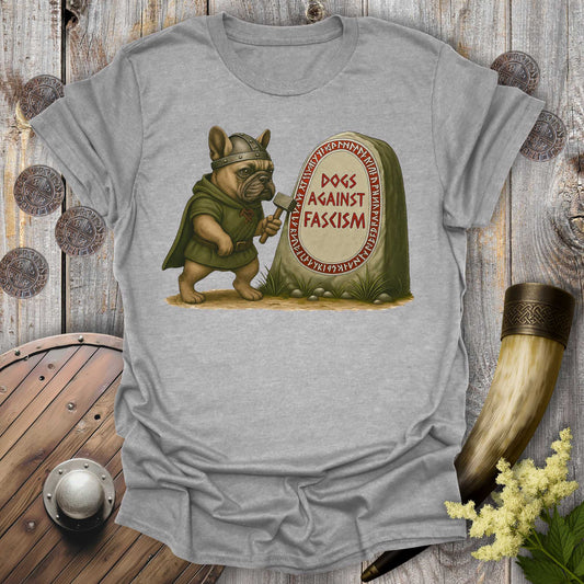 Gray Anti-Fascism No Kings t-shirt with a graphic of a Bulldog in Viking attire holding a hammer next to a stone with "Dogs Against Fascism" text, displayed on a wooden surface.