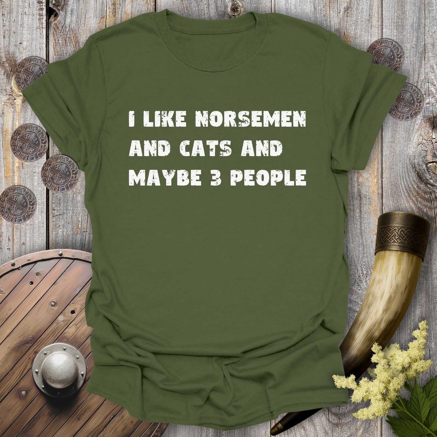 Military Green t-shirt with white distressed text "I Like Norsemen and Cats and Maybe 3 People" on a wooden background.