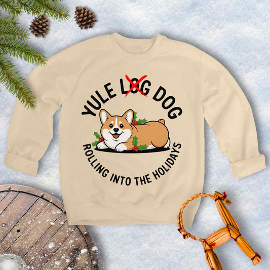 Beige Sand colored sweatshirt with a corgi holiday graphic and text "Yule Log Dog Rolling Into the Holidays" With "Log" crossed over in red, on a snowy background.