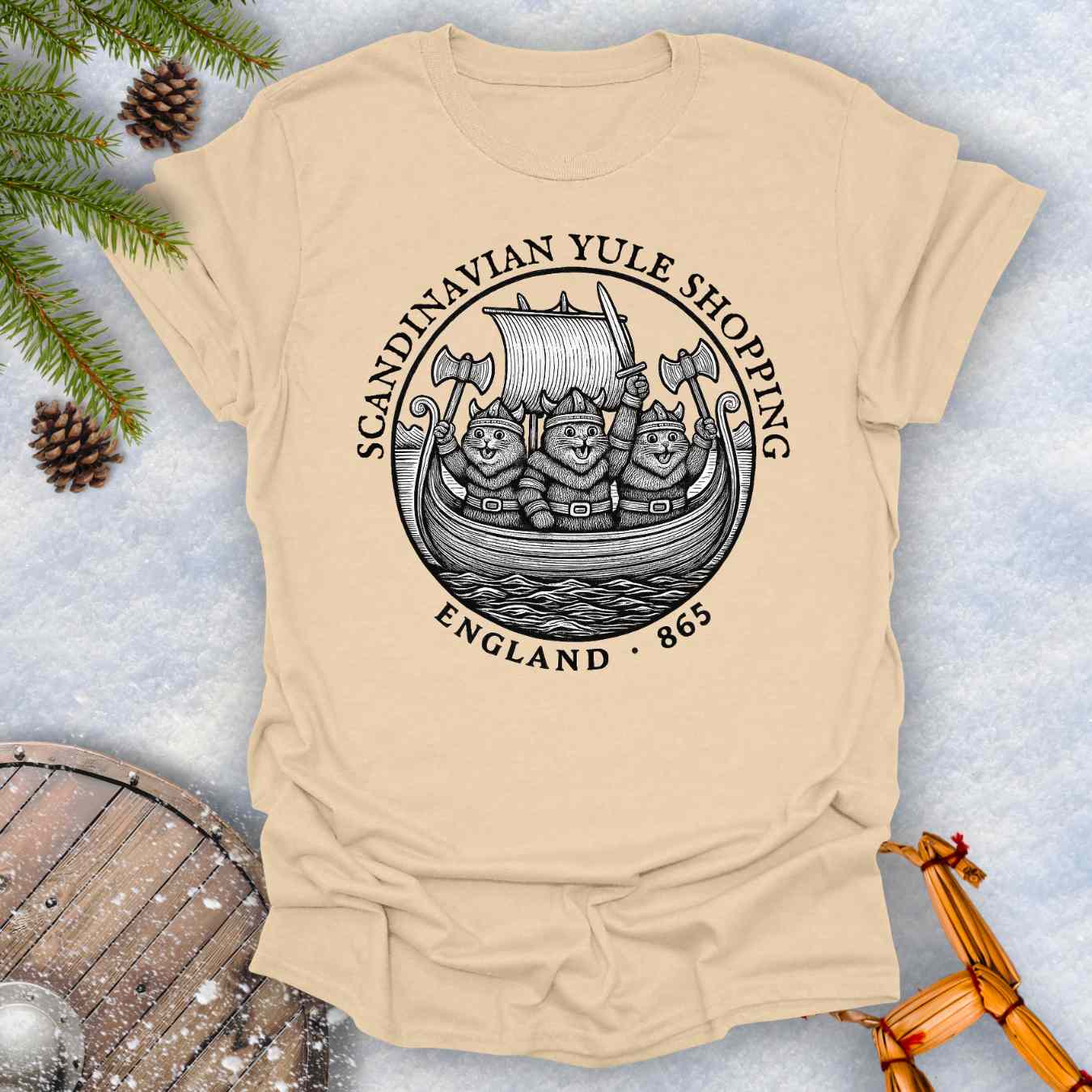 Beige sand colored t-shirt with a black graphic design of Viking cats in a ship. Text: Scandinavian Yule Shopping England 865