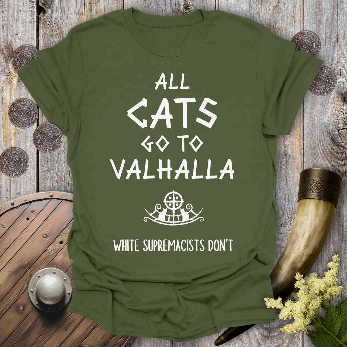 Green t-shirt with 'All cats go to Valhalla, white supremacists don't' text on a wooden background.