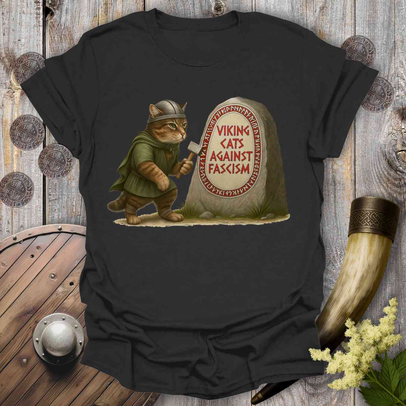 Black t-shirt with a graphic of a cat in Viking attire next to a stone with 'Viking Cats Against Fascism' text, on a wooden background.