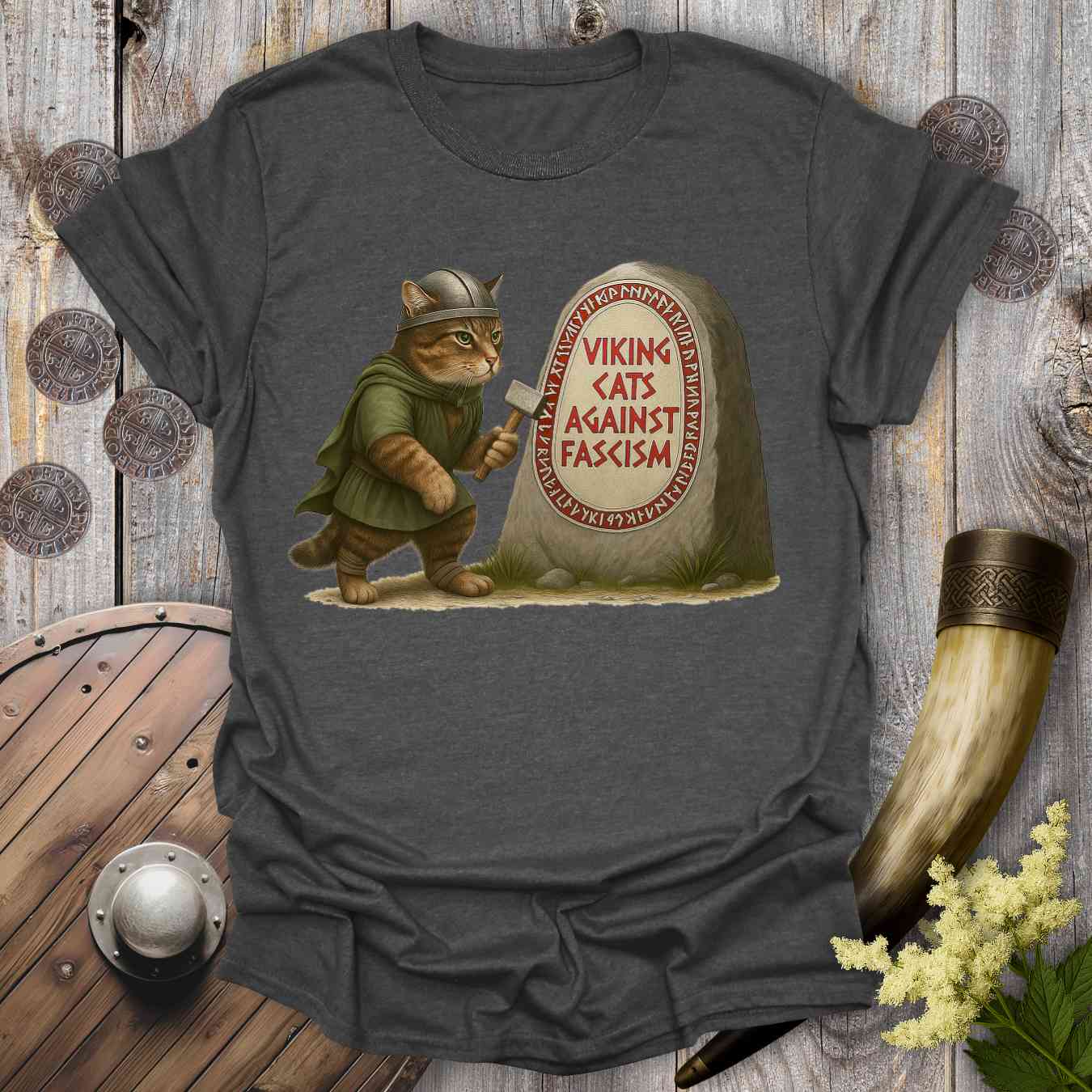 Gray t-shirt with a graphic of a cat in Viking attire next to a stone with 'Viking Cats Against Fascism' text, on a wooden background.
