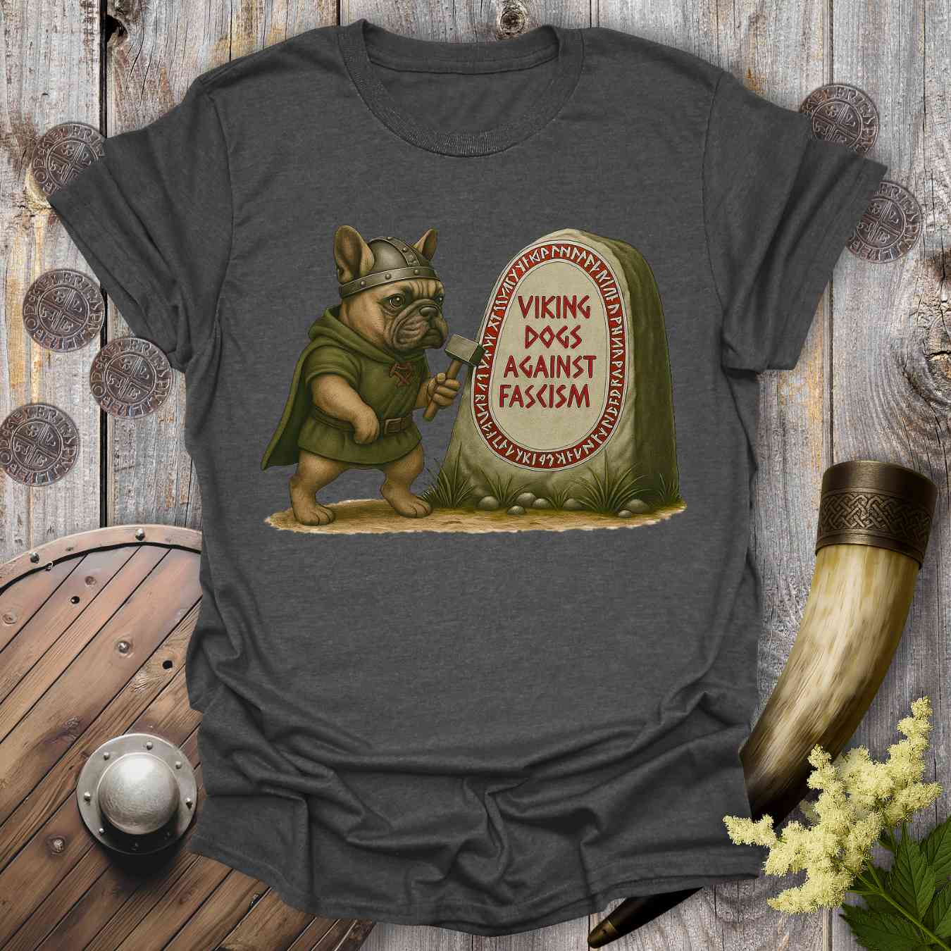 T-shirt with a Viking-themed graphic of a dog holding an ax and a stone with text 'viking dogs against fascism'. Placed on a wooden background.