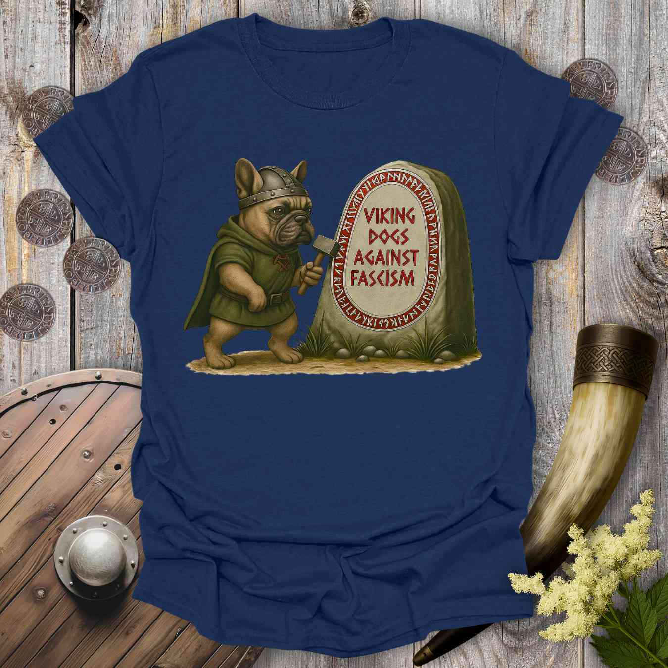 Blue t-shirt with a graphic of a dog in Viking attire holding an ax, standing next to a stone with 'Viking Dogs Against Fascism' text, on a wooden background.
