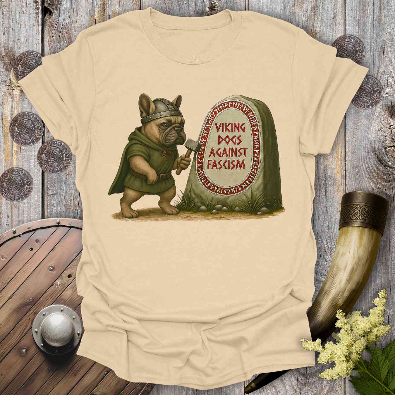 Beige t-shirt with a graphic of a dog in Viking attire holding an axe, standing next to a stone with 'Viking Dogs Against Fascism' text, on a wooden background.