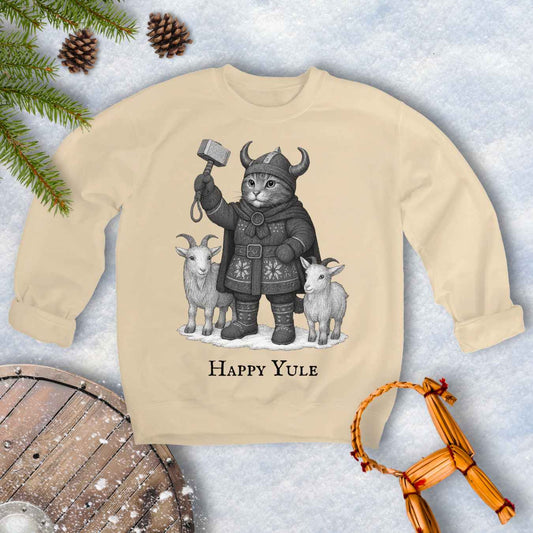 Beige Sand colored sweatshirt with a black and white graphic of a Viking cat in winter gear, holding hammer Mjölnir, surrounded by two goats. 'Happy Yule' text under the image.