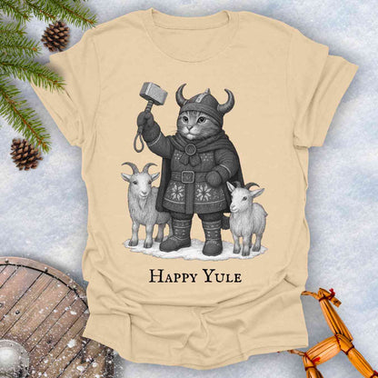 Beige Sand colored t-shirt with a black and white graphic of a Viking cat in winter gear, holding hammer Mjölnir, surrounded by two goats. 'Happy Yule' text under the image.