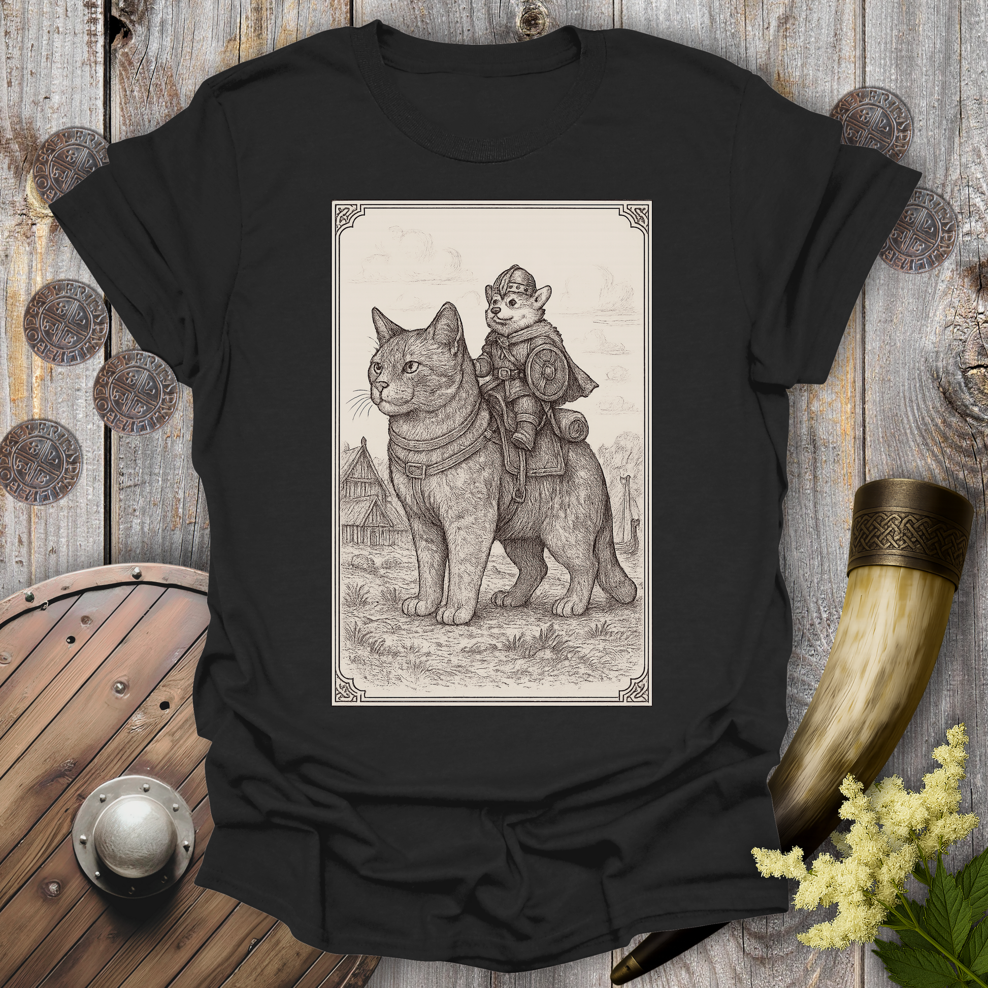 Black t-shirt with a beige and black graphic of a large cat and a Corgi Viking Dog riding it, in a Medieval Viking Age setting. 