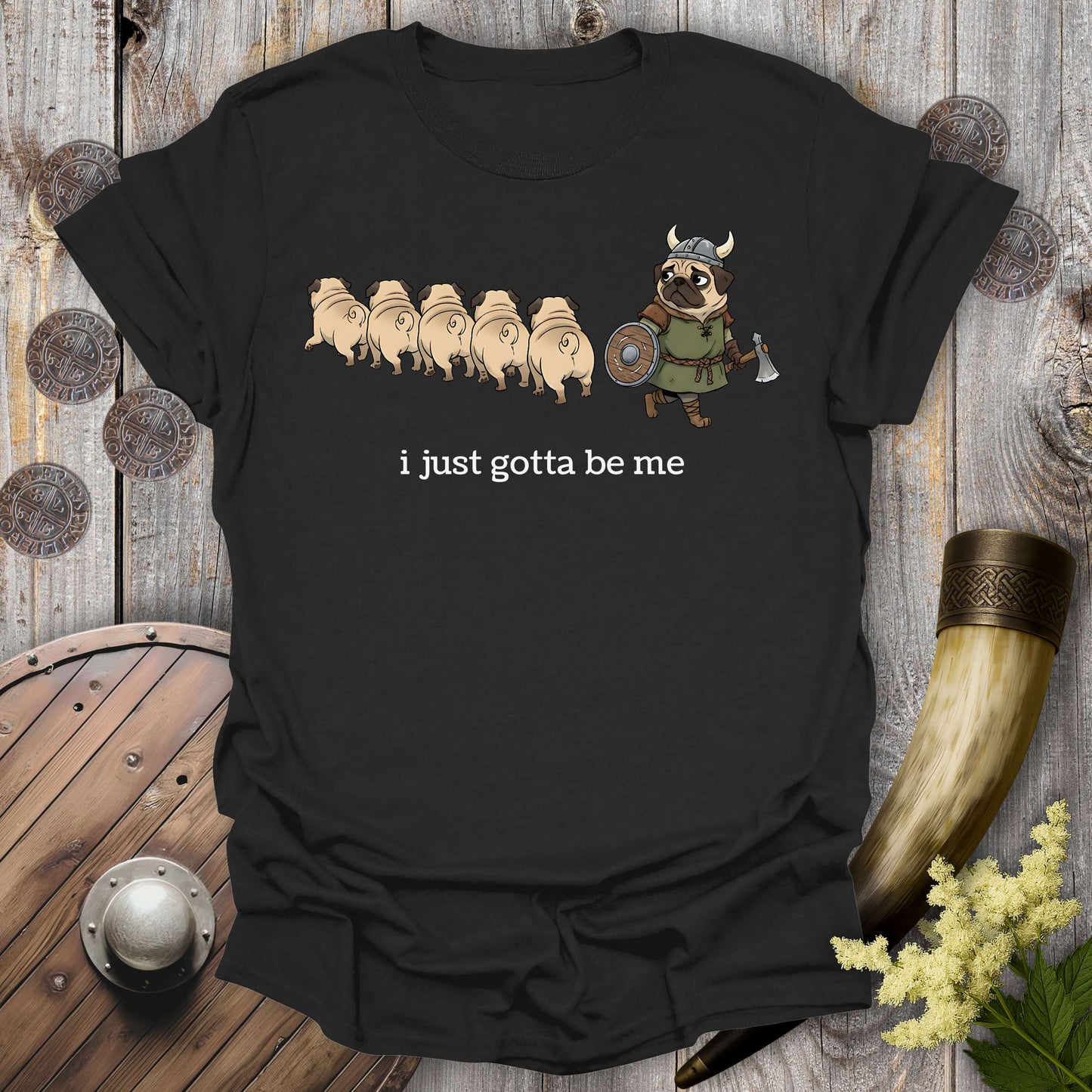 Black t-shirt with cartoon Viking pug design and text "i just gotta be me" on a wooden background.