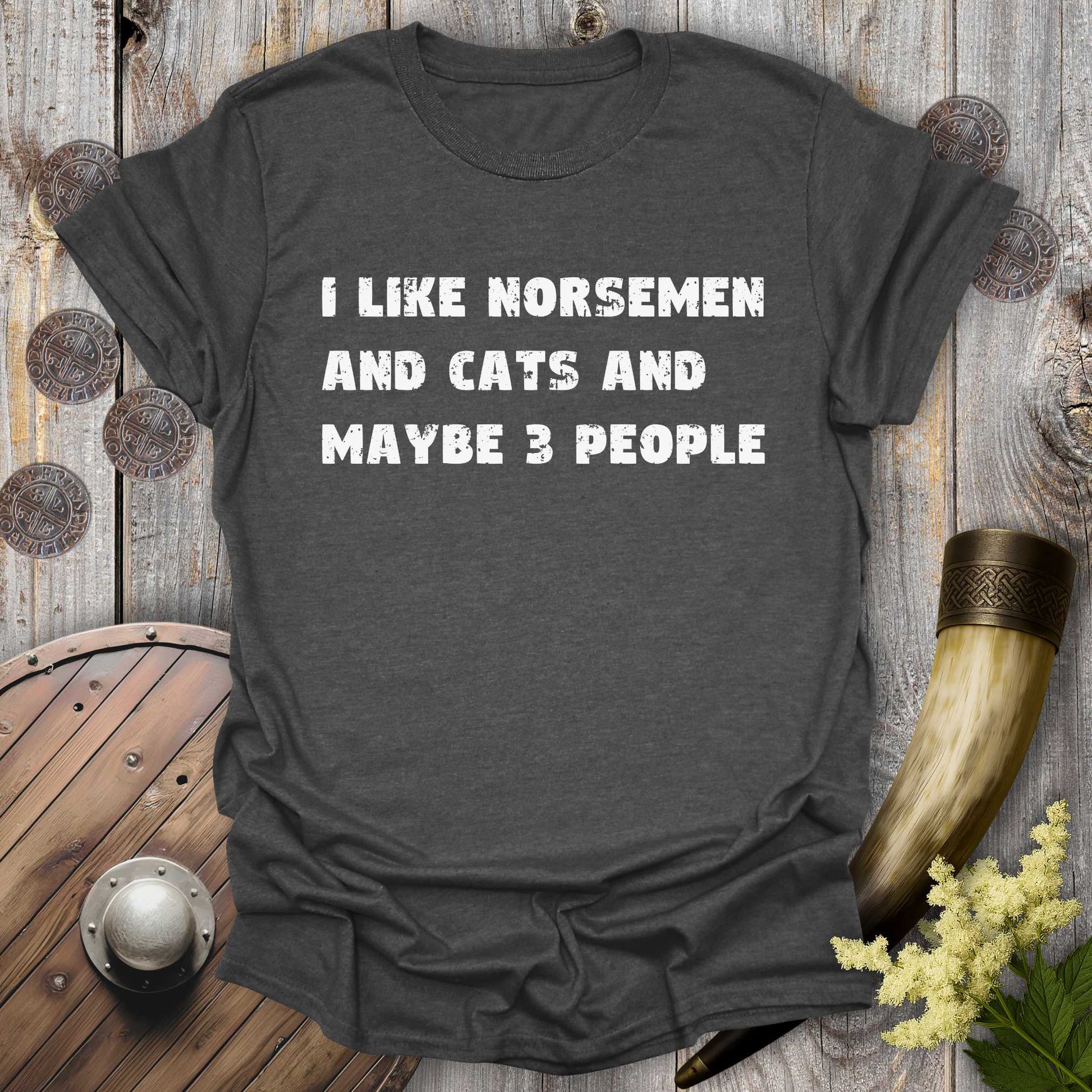 Gray dark heather t-shirt with white distressed text "I Like Norsemen and Cats and Maybe 3 People" on a wooden background.
