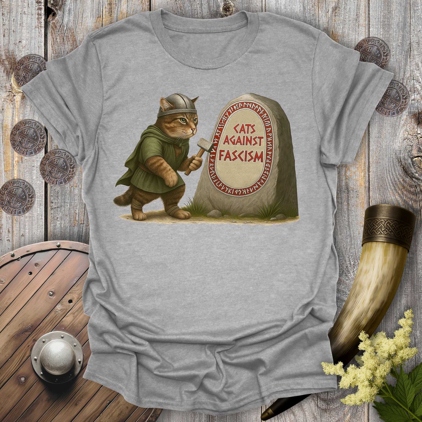 Gray t-shirt with a graphic of a cat in Viking attire holding an axe next to a stone with 'Cats Against Fascism' text, displayed on a wooden surface.