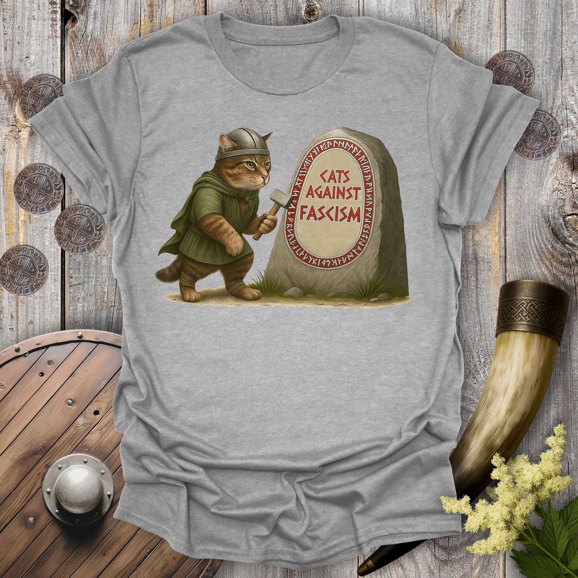 Gray t-shirt with a graphic of a cat in Viking attire holding an axe next to a stone with 'Cats Against Fascism' text, displayed on a wooden surface.