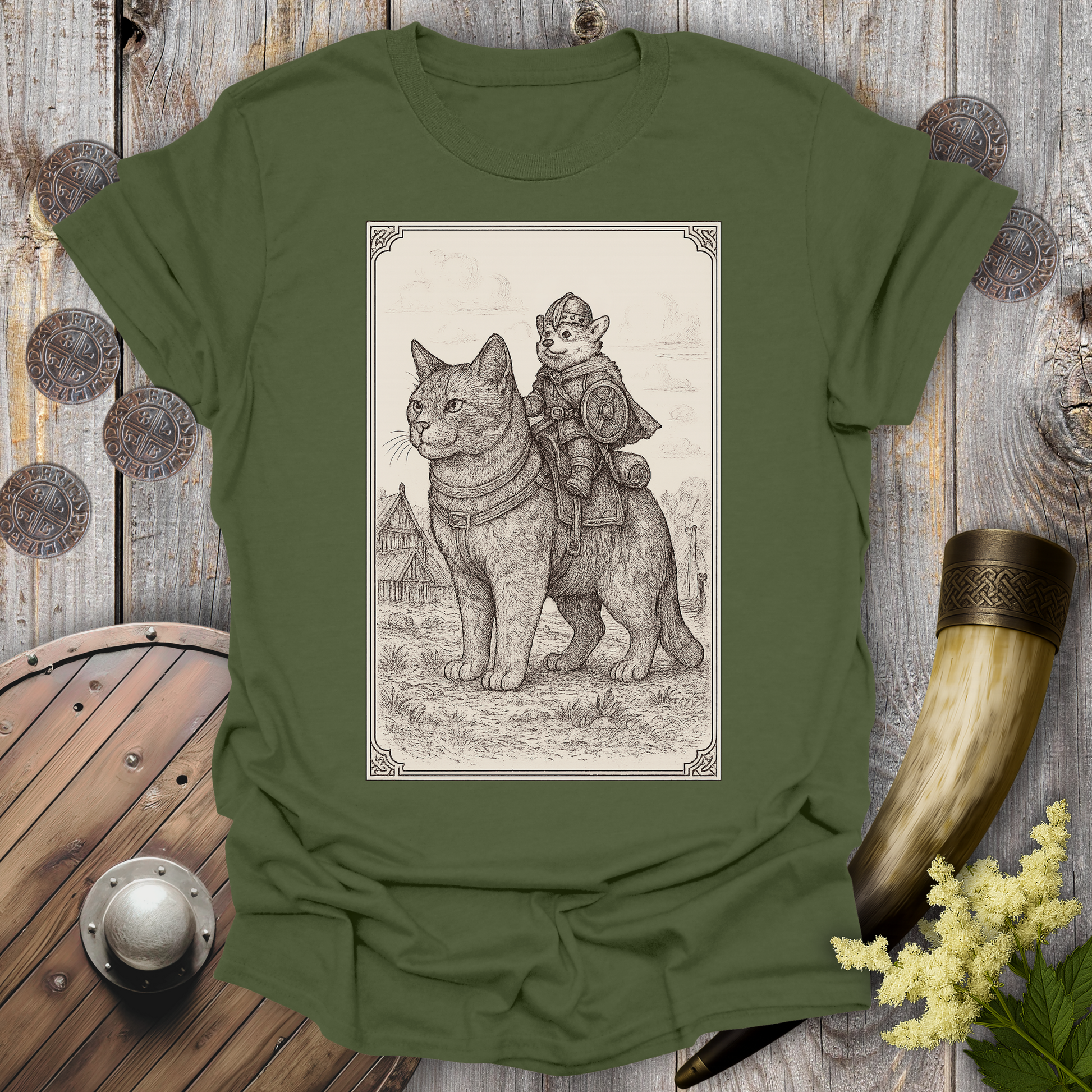 Green t-shirt with a beige and black graphic of a large cat and a Corgi Viking Dog riding it, in a Medieval Viking Age setting. 