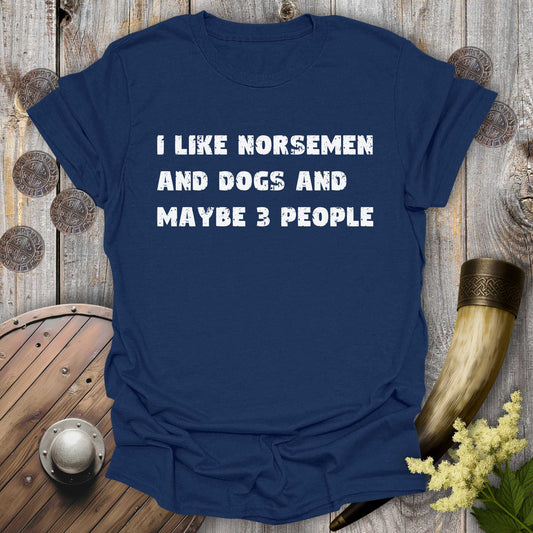 Navy blue t-shirt with white distressed text "I Like Norsemen and Dogs and Maybe 3 People" on a wooden background.