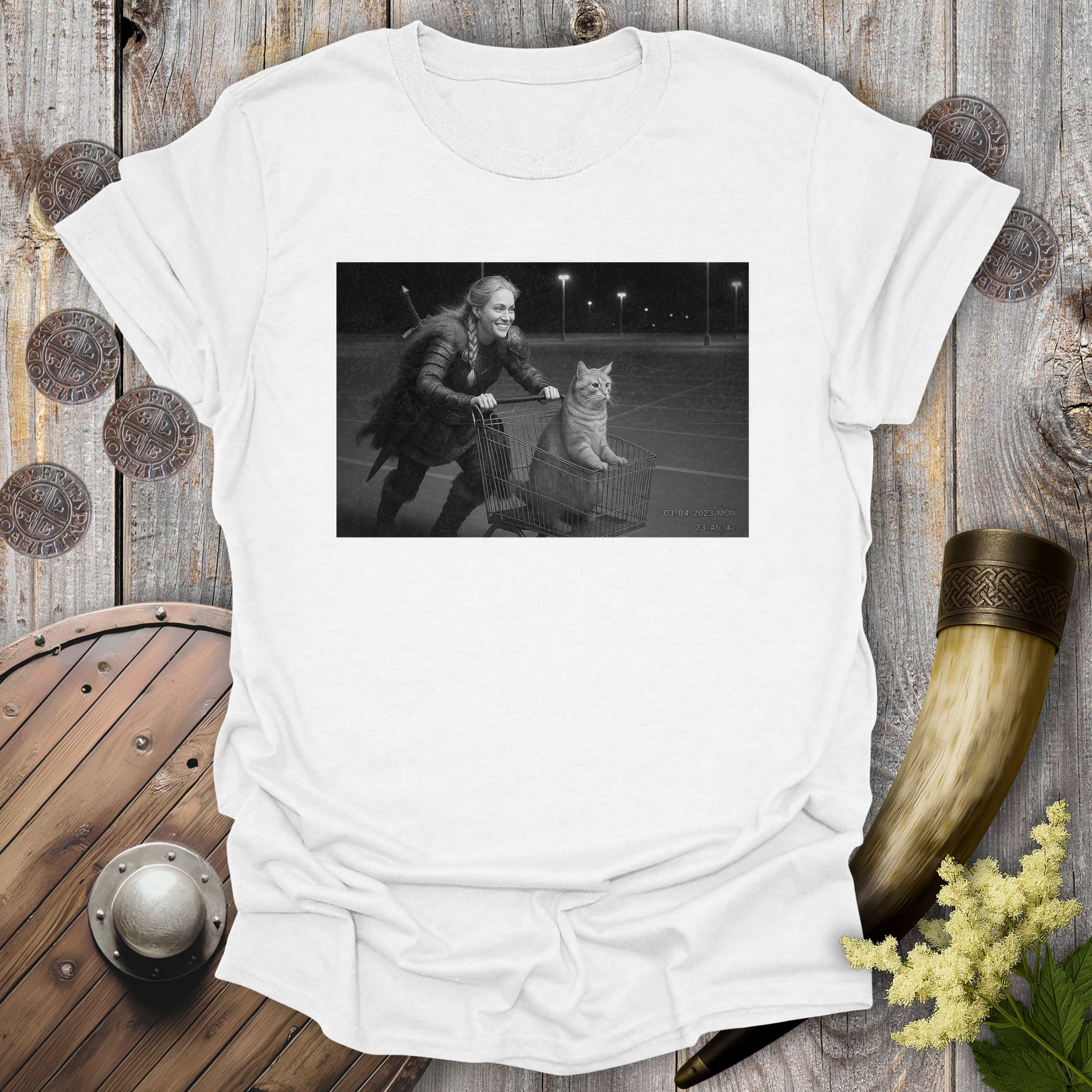 White t-shirt with a graphic of a Viking Shieldmaiden and a tabby cat in a shopping cart, sprinting on a parking Lot.