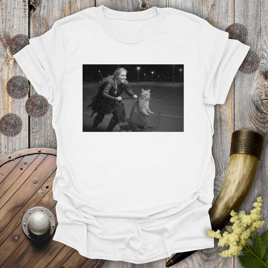 White t-shirt with a graphic of a Viking Shieldmaiden and a tabby cat in a shopping cart, sprinting on a parking Lot.