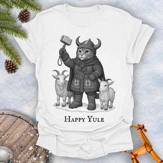 White t-shirt with a black and white graphic of a Viking cat in winter gear, holding hammer Mjölnir, surrounded by two goats. 'Happy Yule' text under the image.