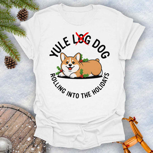 White T-Shirt with a Corgi holiday graphic and text "Yule Log Dog Rolling Into the Holidays" With "Log" crossed over in red, on a snowy background.