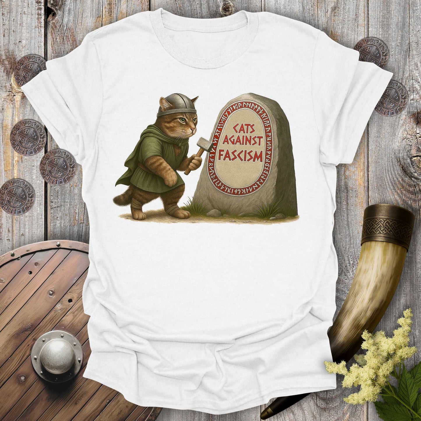 White t-shirt with a graphic of a cat in Viking attire holding an axe next to a stone with 'Cats Against Fascism' text, displayed on a wooden surface.