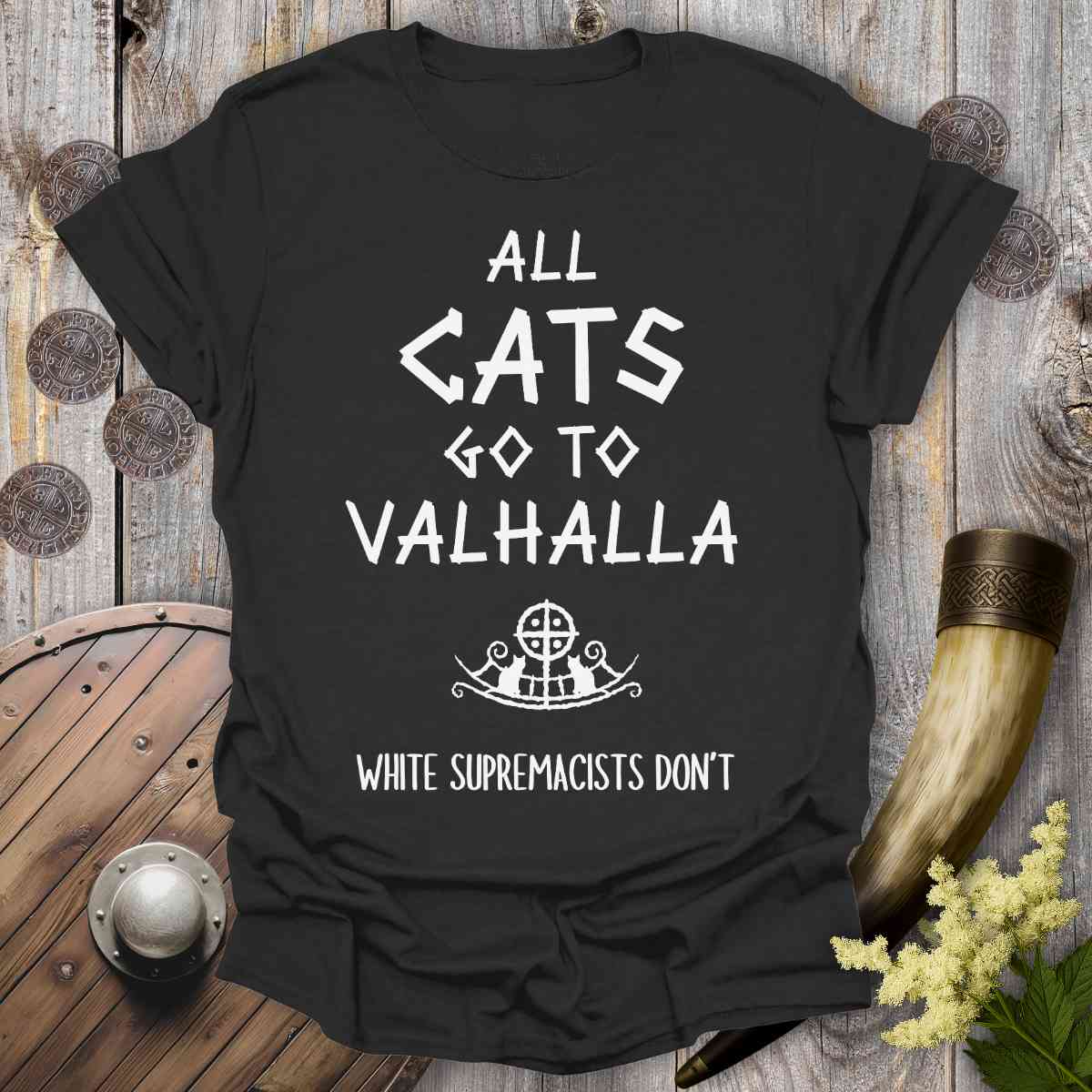 Black t-shirt with 'All cats go to Valhalla, white supremacists don't' text on a wooden background.