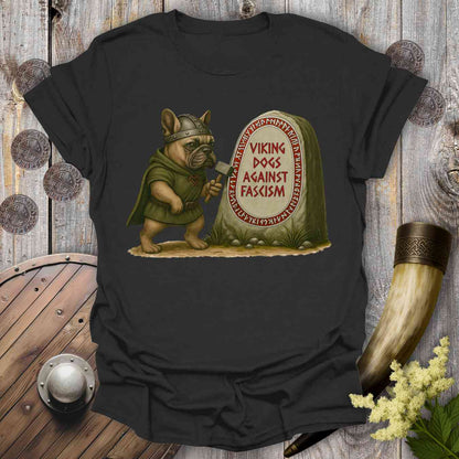 Black t-shirt with a graphic of a dog in Viking attire next to a gravestone with 'Viking Dogs Against Fascism' text, on a wooden background.