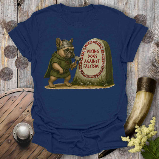 Blue t-shirt with a graphic of a dog in Viking attire holding an ax, standing next to a stone with 'Viking Dogs Against Fascism' text, on a wooden background.