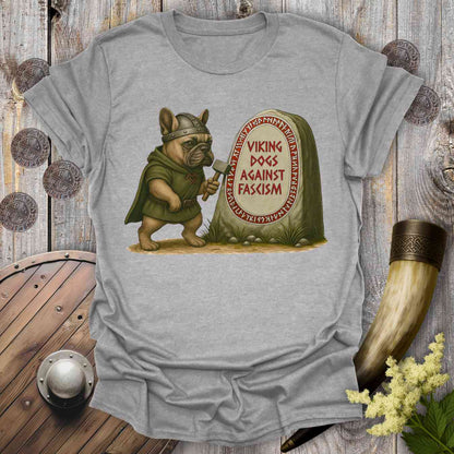 Gray t-shirt with a graphic of a dog in Viking attire holding an ax, standing next to a stone with 'Viking Dogs Against Fascism' text, on a wooden background.