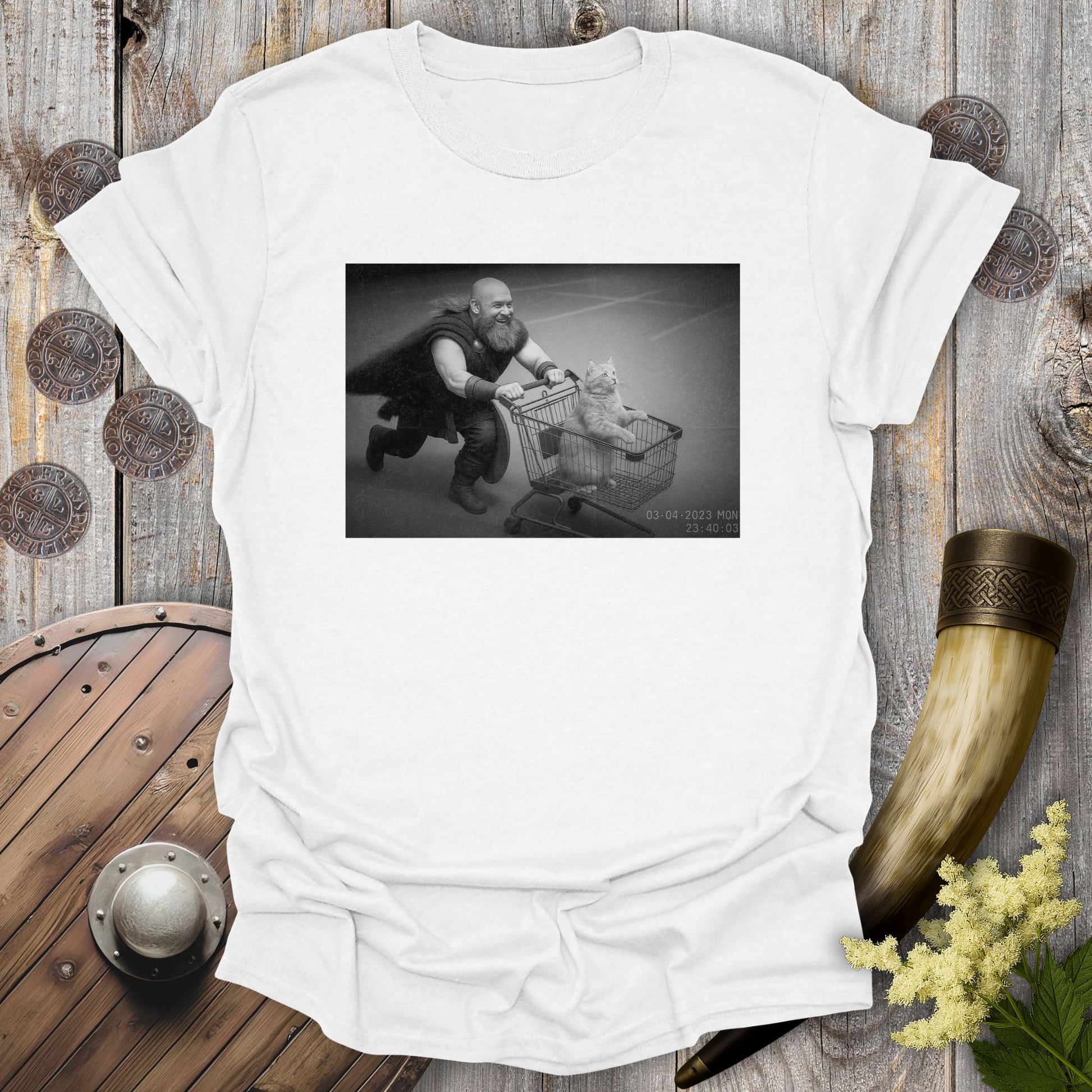 White t-shirt with a graphic of a Viking and a cat in a shopping cart, sprinting on a parking Lot.